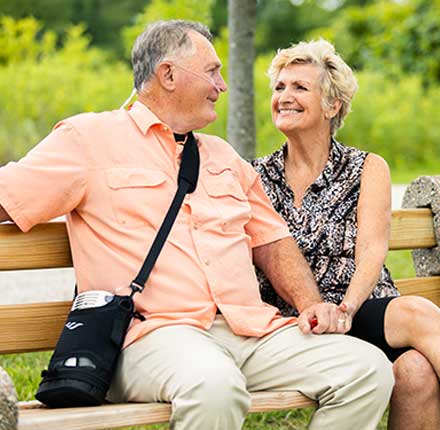 Couple on a park bench, he wears a portable oxygen concentrator